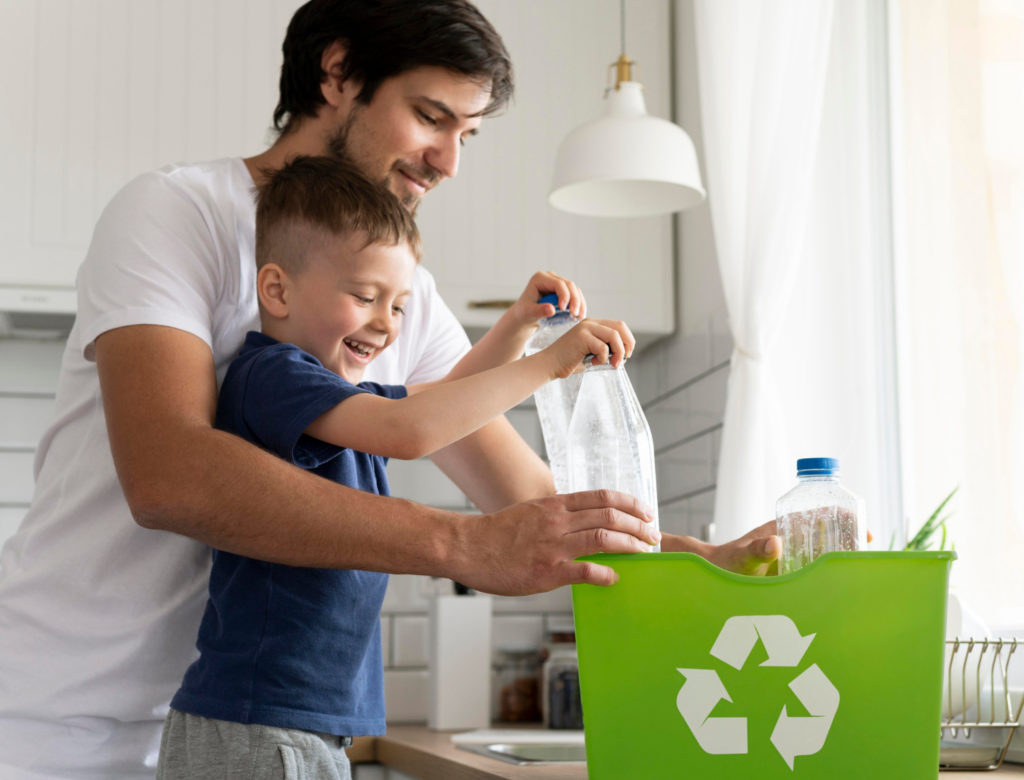 Foto de pai e filho guardando garrafas de plástico em uma sacola verde, estampada com o símbolo de reciclagem, um exemplo de aplicação de logística reversa.